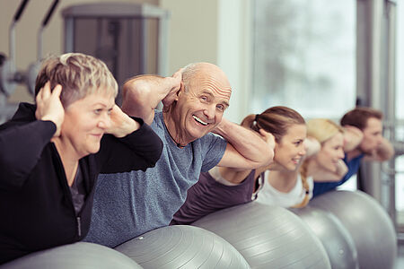 Ein Senior macht Sport in der Gruppe mit Gymnastikbällen