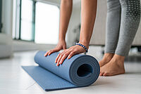 Die Beine einer Person mit zusammengerollter Yoga-Matte sind zu sehen.